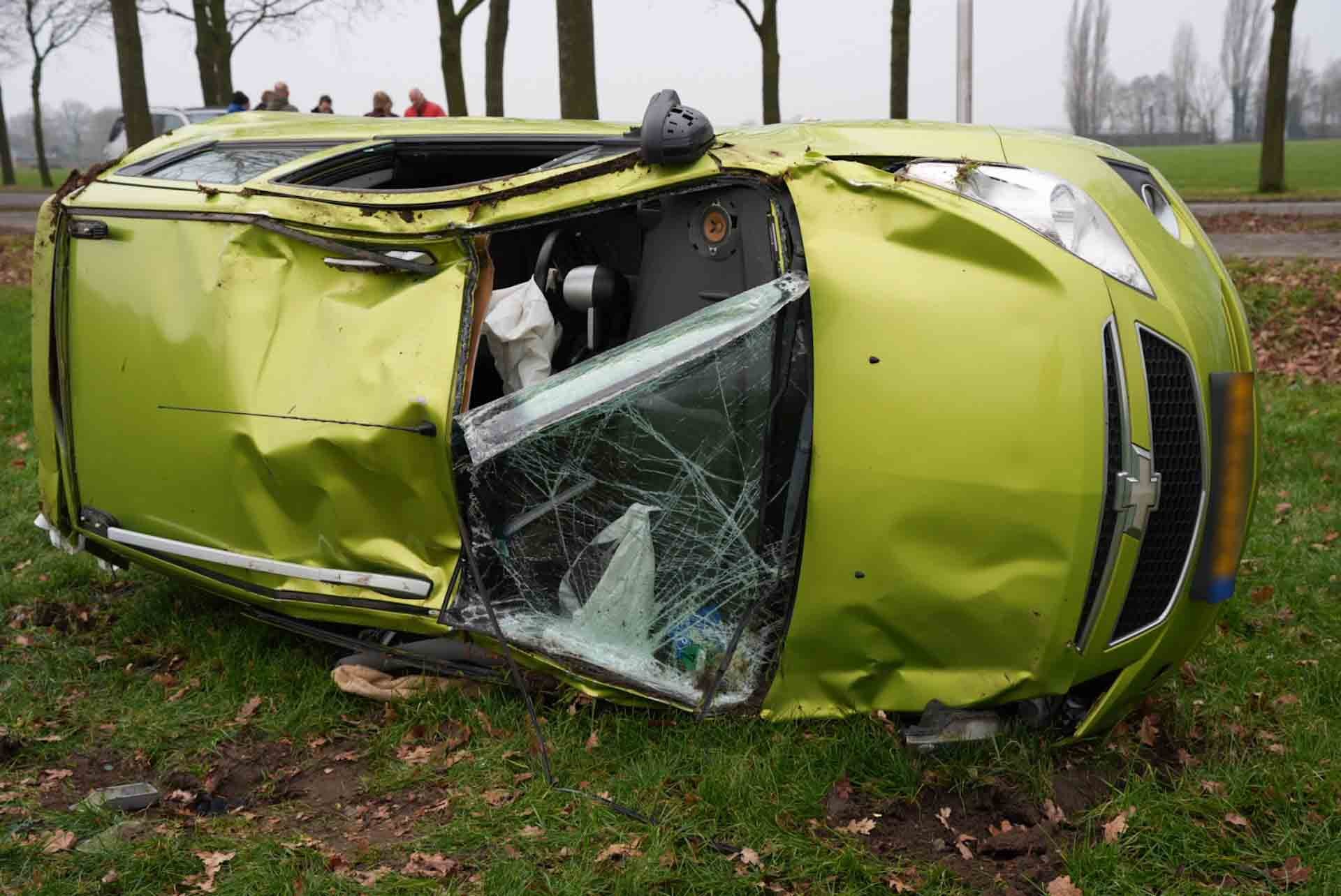 Auto botst tegen boom en belandt op zijkant in weiland