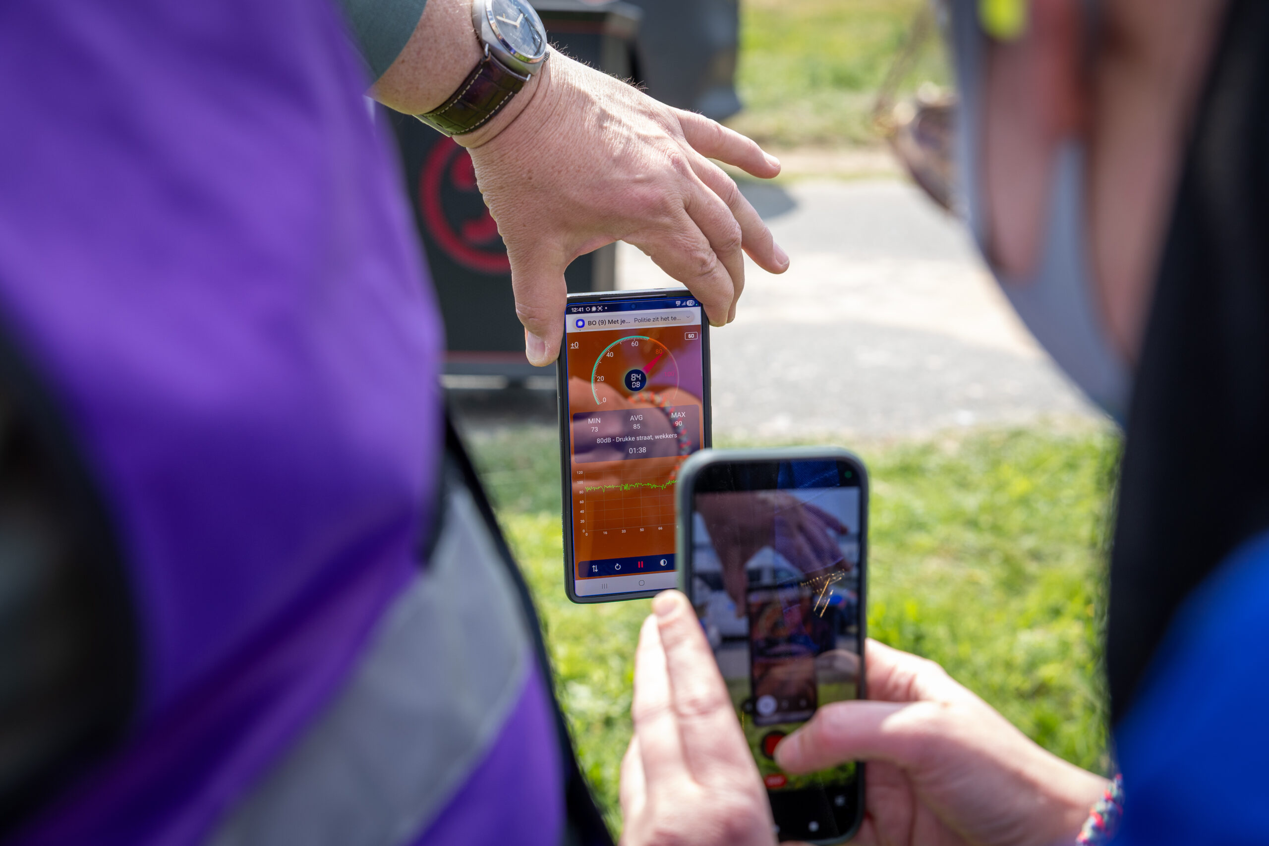 Close-up of a smartphone screen showing a circular gauge, held by hands outdoors.