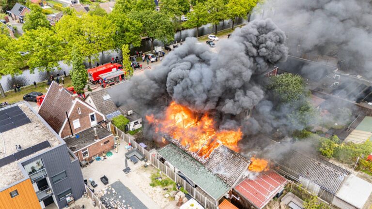 Schuur in as door grote brand, rookwolken zichtbaar in wijde omgeving