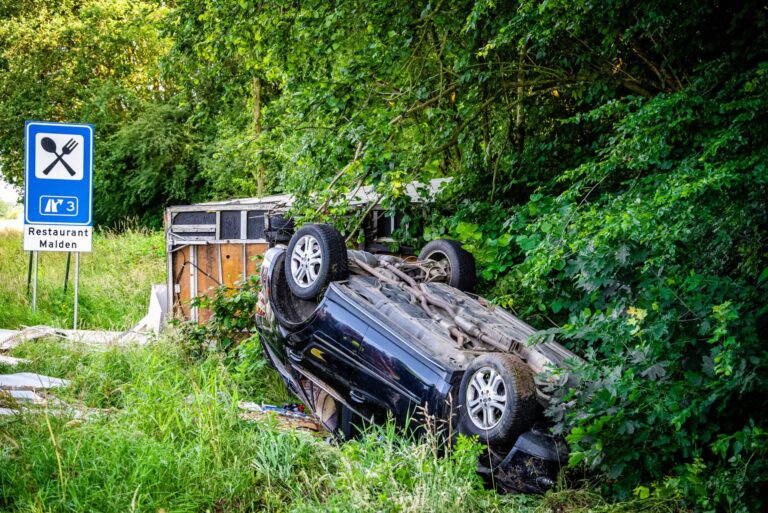 Auto met aanhanger ondersteboven in berm na crash
