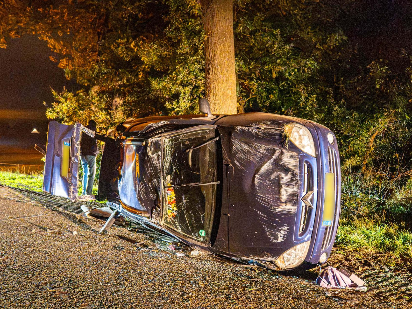 Auto over de kop na botsing tegen boom